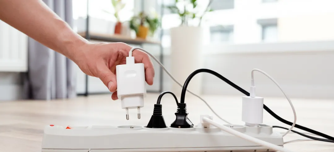 Persona enchufando un cargador en una regleta llena de cables