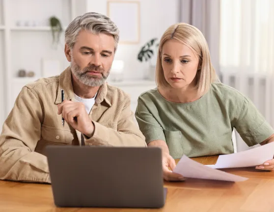 Pareja adulta comparando documentos físicos y en el ordenador