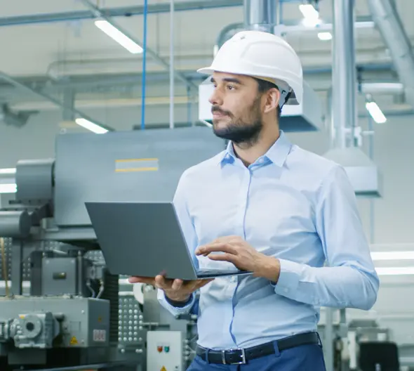 chico con casco y ordenador en una fábrica