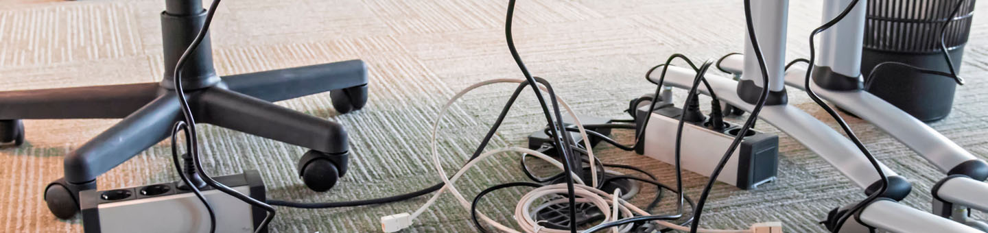 Muchos cables conectados a enchufes debajo de un puesto de trabajo